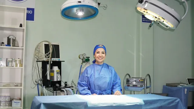 Una cirujana con gorro y bata azul sonríe detrás de la mesa del quirófano, bajo las lámparas
